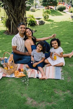 A joyful family enjoys a sunny picnic with fresh bread and juice on a green park blanket.
